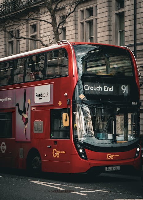 Photograph of a red double-decker bus parked on a city street with historic stone buildings in the background. The bus displays ‘Crouch End’ on its digital route sign and features advertising graphics on its side. The scene is illuminated by natural daylight, highlighting the clean and well-maintained exterior of the bus. This image reflects urban transport infrastructure, relevant to residential or commercial environments, and is associated with the services provided by Cleaners Haringey in the context of end of tenancy cleaning and surface sanitation.