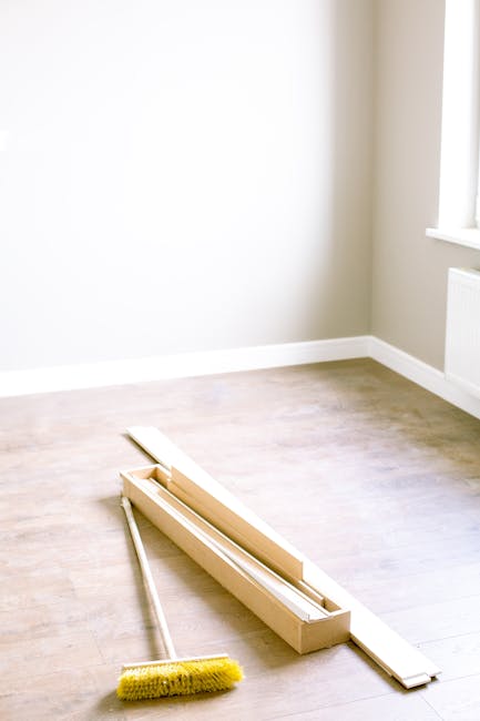 A close-up view of a broom and dustpan set on a wooden floor, with the broom's beige bristles and wooden handle prominently displayed. The dustpan is black with a wooden lip that matches the broom handle, positioned behind the broom. The scene highlights a clutter-free, clean floor surface prepared for sweeping, with soft, natural lighting emphasizing the smoothness of the wood. The background features a blurred wooden surface, suggesting a residential or commercial interior. Cleaners Haringey specializes in deep cleaning and surface sanitisation, ensuring thorough hygiene and maintained cleanliness within domestic or commercial spaces.